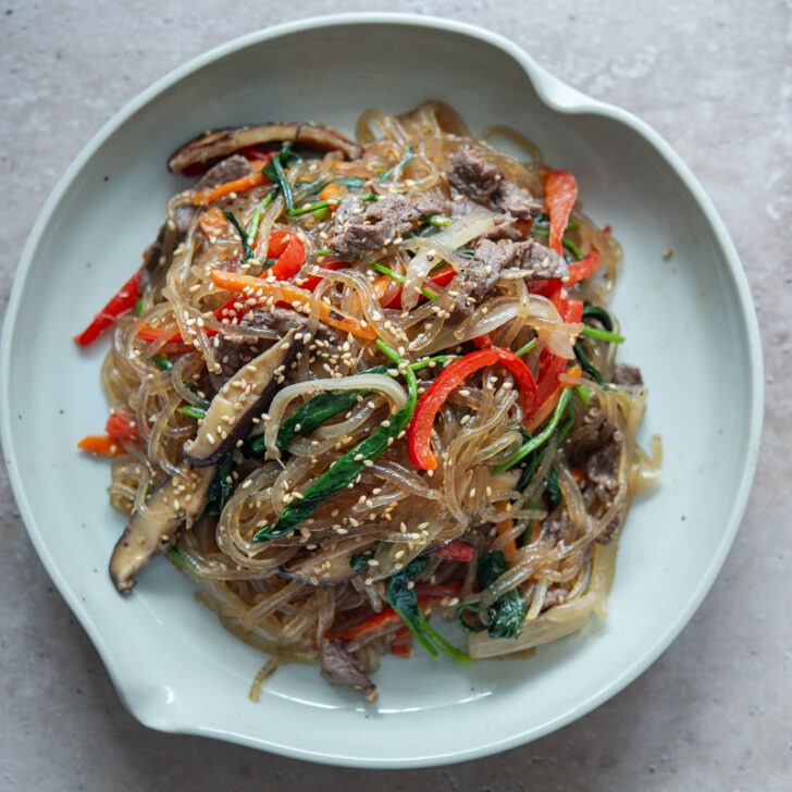 Japchae with colorful veggies and noodles served on a plate.