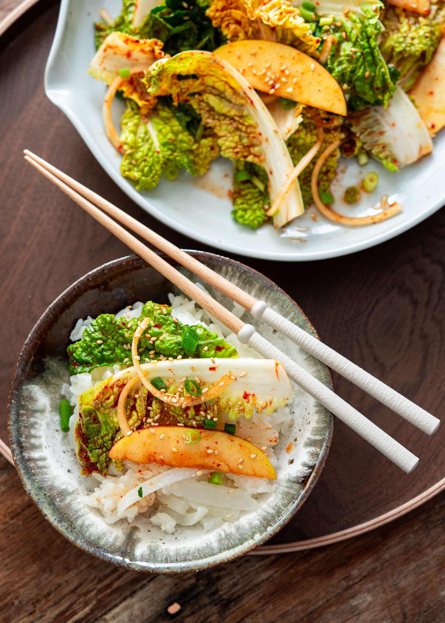A bowl of white rice topped with spicy Bomdong salad and apple slices, served with chopsticks