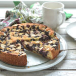 A slice of blueberry cake shows the burst of fresh blueberries on a white plate.