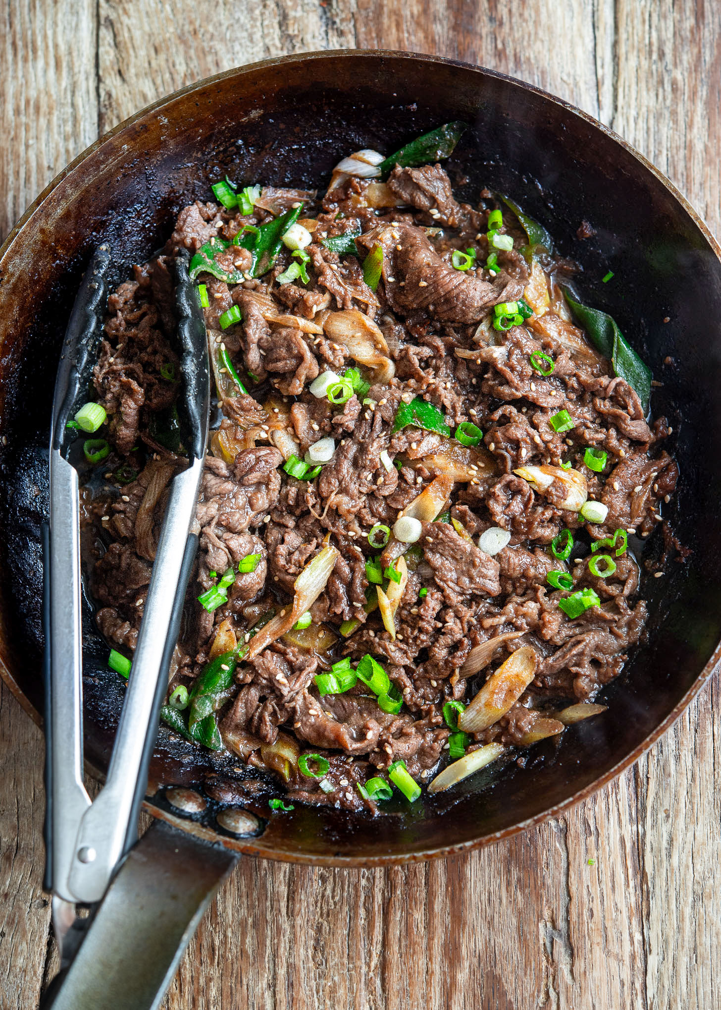 Korean beef bulgogi cooking in a pan with onions and green onion garnish