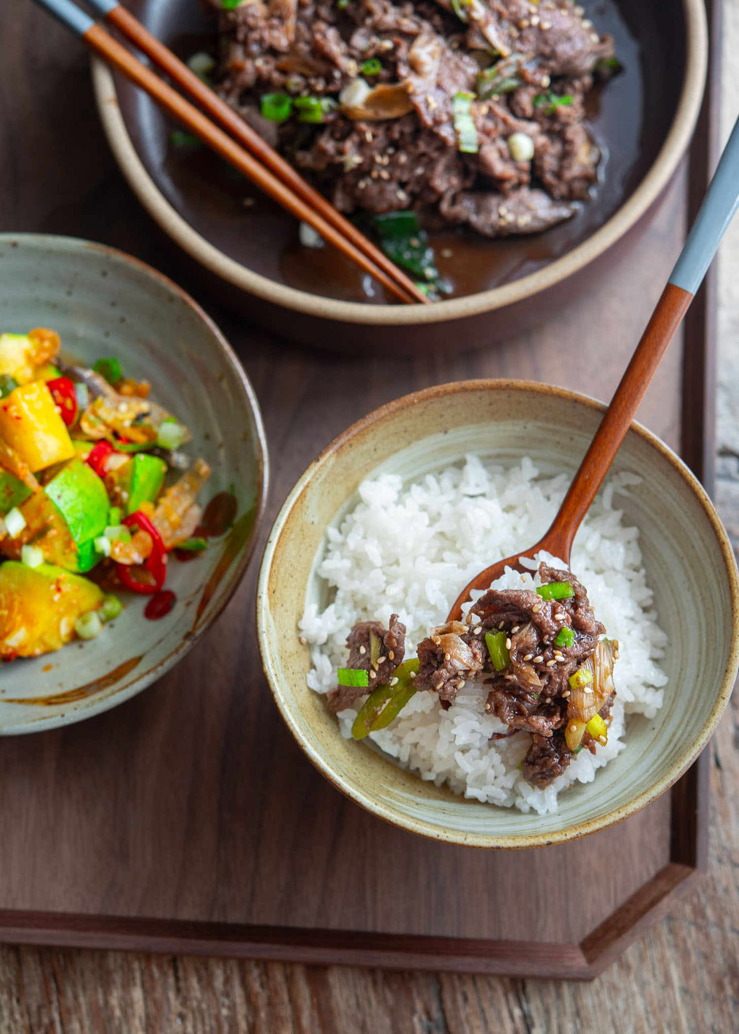 Korean beef bulgogi served over white rice with spoon and side dishes