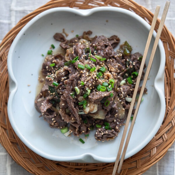 Authentic Korean beef bulgogi in a serving dish topped with chopsticks.