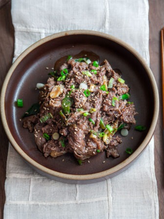 Korean beef bulgogi with glossy caramelized slices and green onion garnish in a brown bowl