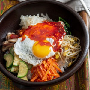 Korean bibimbap with mixed vegetables and fried egg topped with gochujang sauce