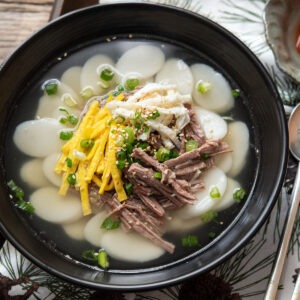 Korean tteokguk rice cake soup with sliced rice cakes, beef, egg, and green onion in clear broth