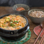 Hot boiling doenjang jjigae in a stone pot is a served with rice and kimchi