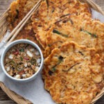 Crispy Korean bindaetteok arranged in a basket with soy dipping sauce and chopsticks