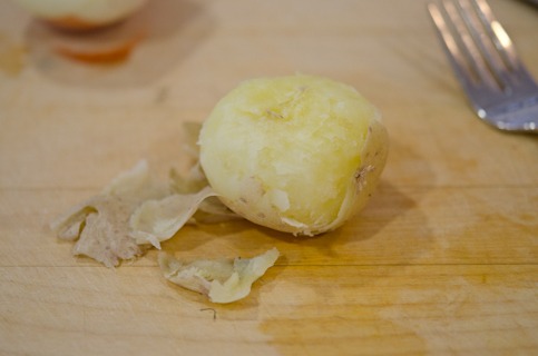 The skin of a small cooked potato is being peeled.
