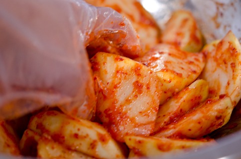 Radish slices are being tossed with kimchi paste by hand.