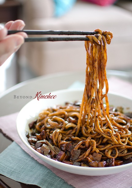 A chopstick is holding strands of jjajangmyeon noodles from the noodle bowl.