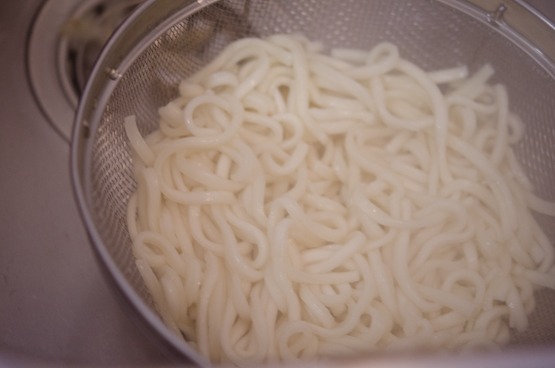 Cooked noodles are draining in a strainer.