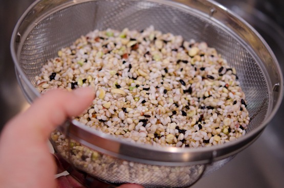 Soaked mixed grains are drained in a mesh colander.