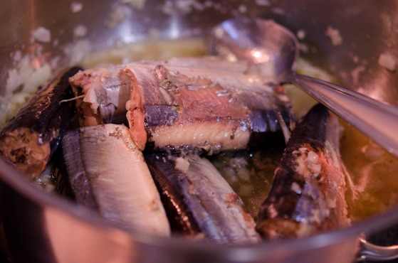 Canned mackerel pike is added to the onion garlic mixture in a pan.