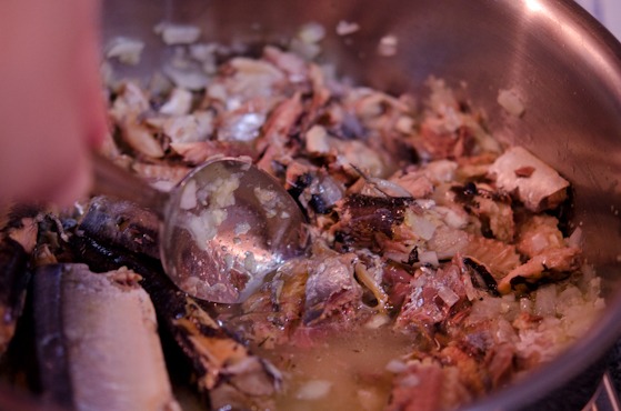 Canned mackerel is being cut with a side of spoon in a pot.