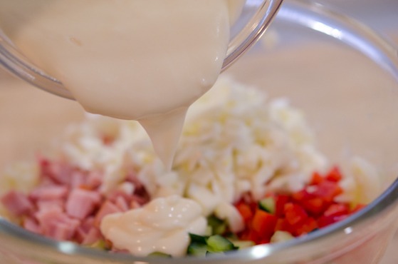 Yogurt dressing is poured on Korean potato salad mixture.