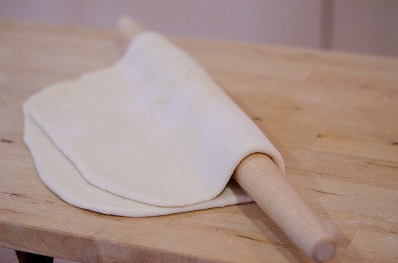 A rolling in is about to carry the rolled pizza dough to a baking pan.