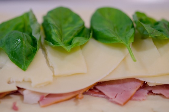 Cheese slices and basil leaves are topped over cured meat for Stromboli.