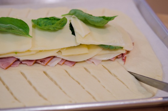 A knife is give some slits on the side of pizza dough to create strips.