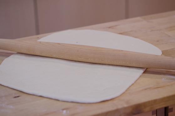 A pizza dough is rolled out with a rolling pin to make Stromboli.