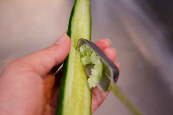 A spoon is used to scoop off the seeds from a cucumber.