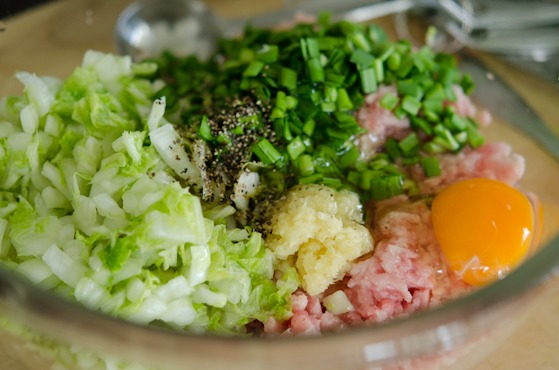 Minced pork is combined with cabbage, chives, garlic and egg in a bowl.