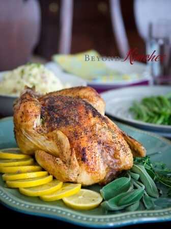 Lemon herb chicken roast is garnished with lemon slices and sage herb on a platter.