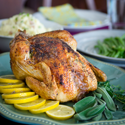 Chicken roast is garnished with lemon slices and sage herb on a platter.