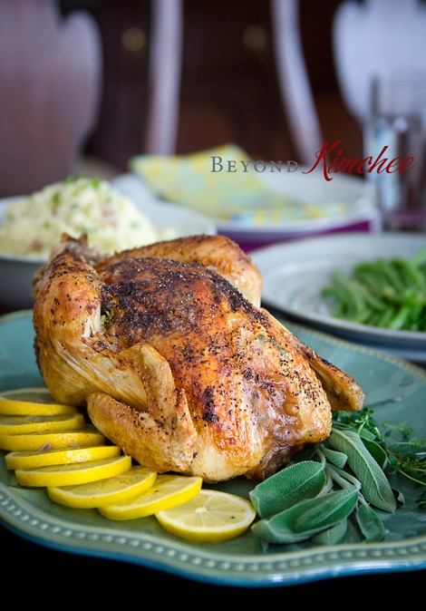 Lemon herb chicken roast is garnished with lemon and sage herb on a platter.