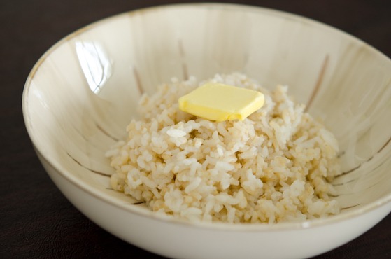 A thin slice of butter is topped over rice in a bowl.