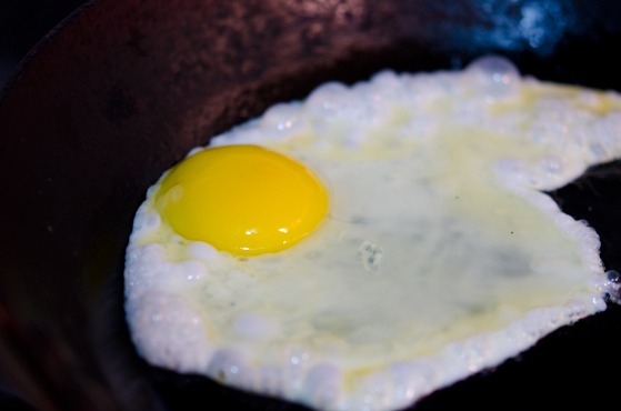 An egg is cracked onto a hot oil in a skillet