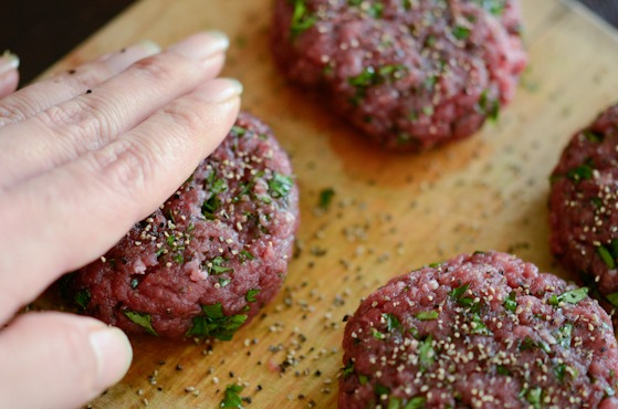 Gently press black peppercorn to the surface of beef patties with a hand.