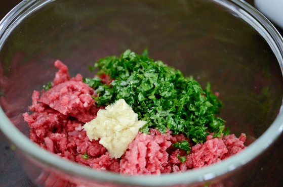 Ground beef, parsley, and garlic is combined in a bowl.