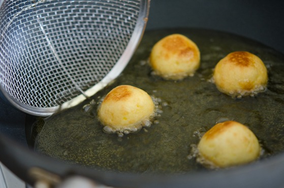 Donut balls are being rolled with a strainer while deep-frying.