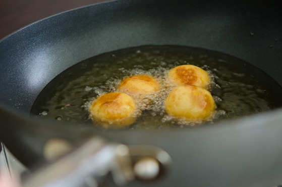Sweet potato rice donut balls are deep frying in oil to golden brown.