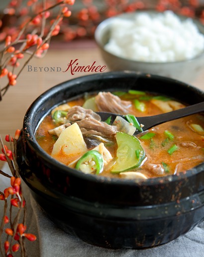 A spoon is dishing up doenajng jjigae with beef and vegetables from the stone pot to show.