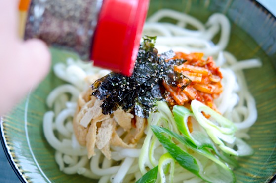 Udon noodle bowl is garnished with kimchi, roasted seaweed, fried bean curd.