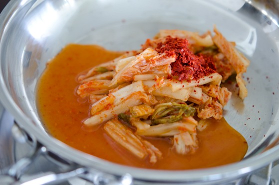 Slices of sour kimchi and Korean chili flakes are placed on a skillet.