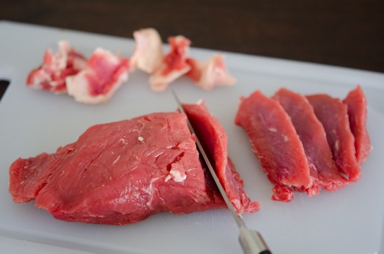 Beef is thinly sliced on the cutting board.