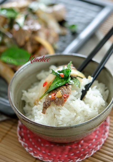 A slice of Thai beef basil stir-fry is served over a bowl of jasmin rice.