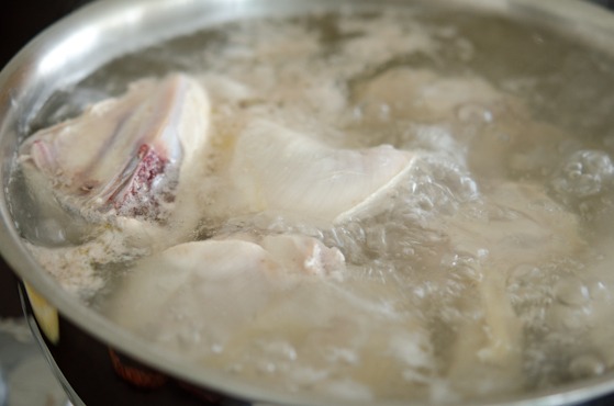 Chicken pieces are par-boiled in a pot.