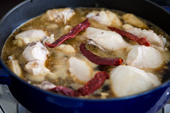 Chicken pieces and dried chili are added to the cola sauce in a pot.