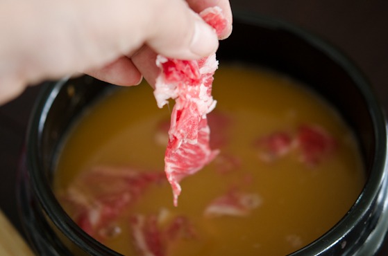 Thin slices of beef is added to Korean soybean paste stock in a stone pot.