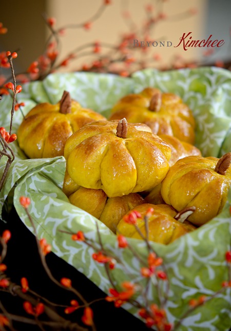 Pumpkin dinner rolls are placed in a basket lined with a patterned green napkin.