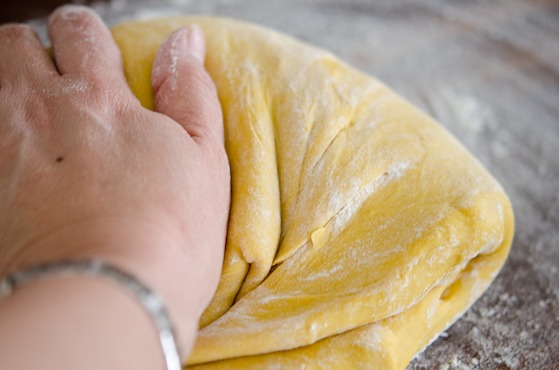 Pumpkin dinner roll dough is kneaded by hand on the floured surface.