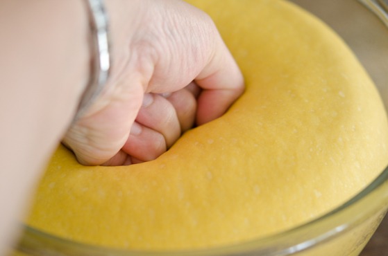A fist is punching the dinner roll dough in a bowl to deflate.