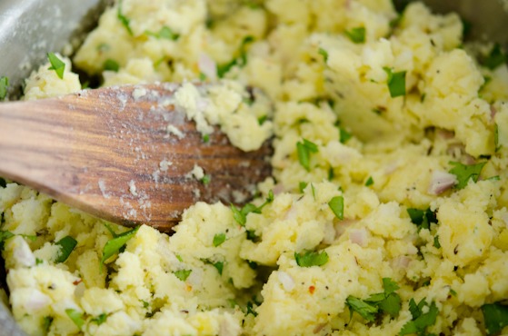 A wooden spatula is mixing mashed potatoes with spice mixture.