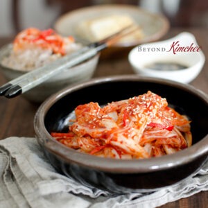 Freshly made kimchi is showing its bright red color and crispy texture in a bowl next to rice.