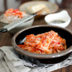 Freshly made kimchi is showing its bright red color and crispy texture in a bowl next to rice.