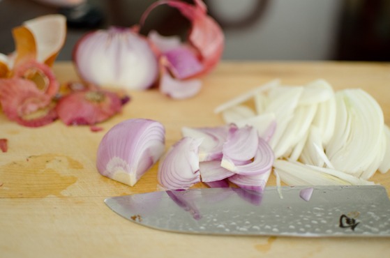A knife is slicing white and red onion.