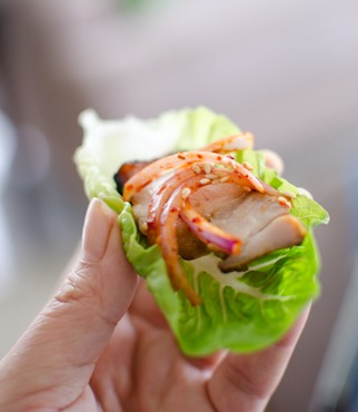 Korean pork belly wrap with oven roasted pork and spicy onion is held by a hand.